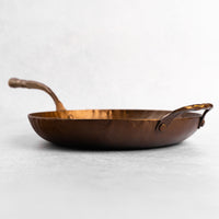 Copper frying pan with handles on a light gray background