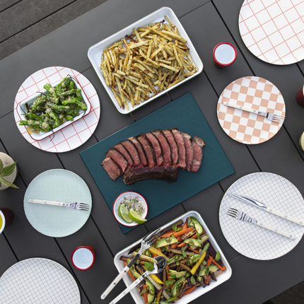 Sliced steak on outdoor table with plates and veggies