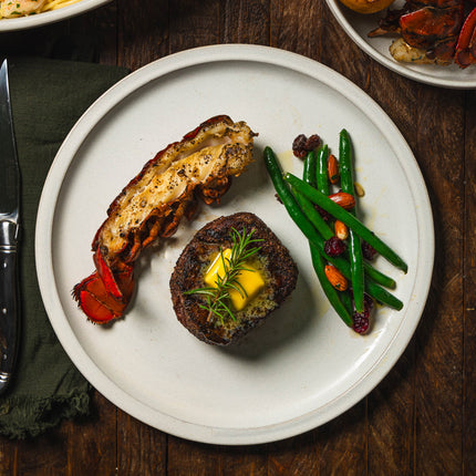 Cooked Steak with butter and rosemary, lobster and veggies on a white plate 