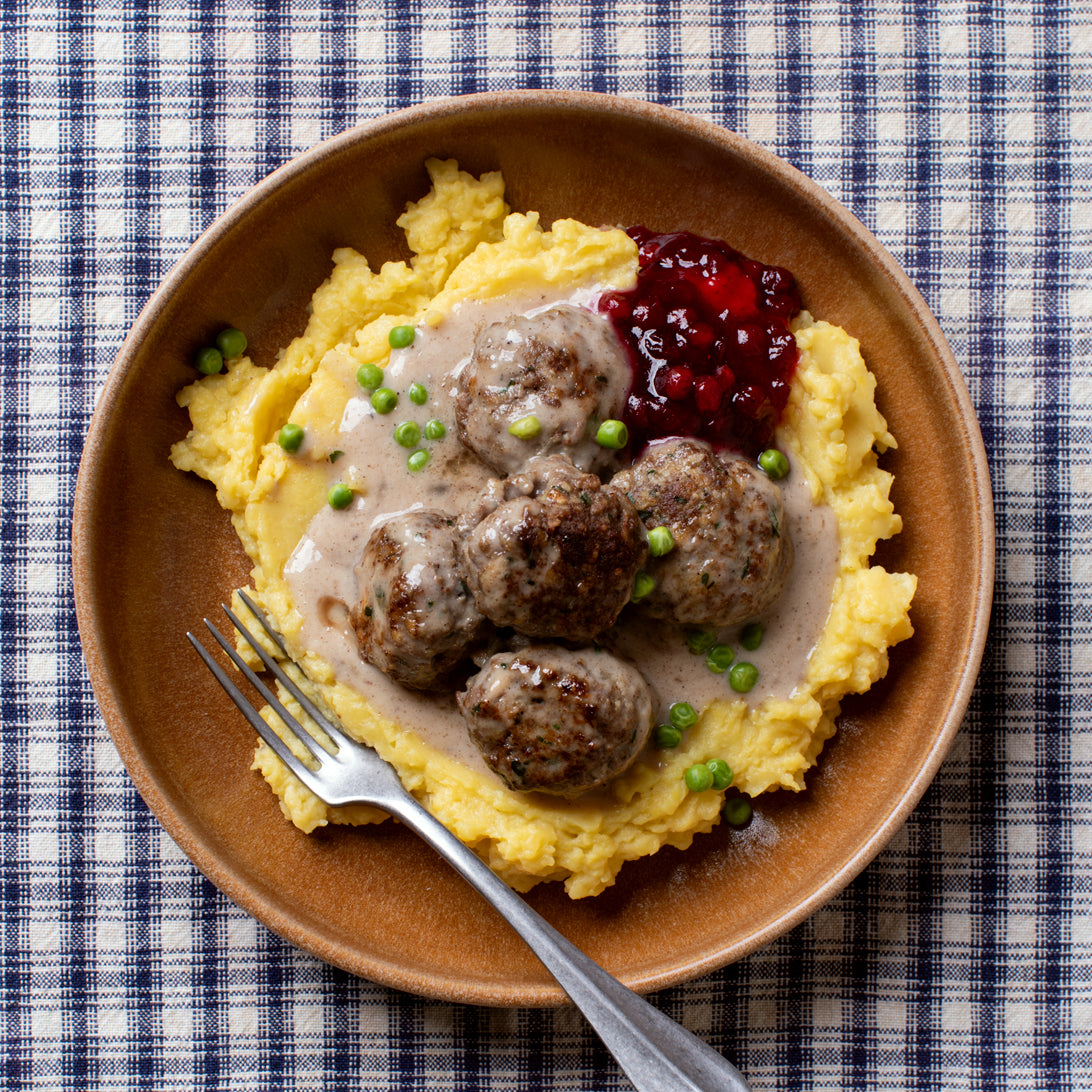 Brown plate with mashed potatoes, meatballs, and cranberry sauce on a checkered tablecloth