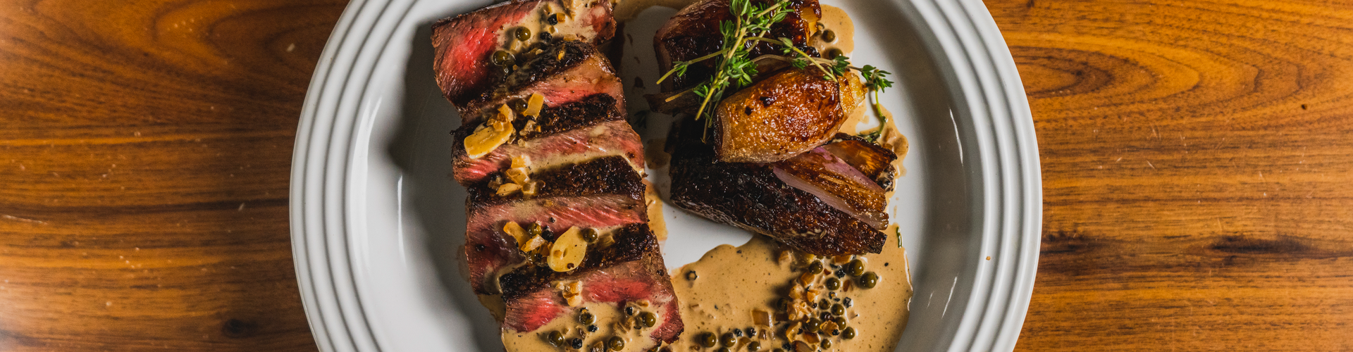 Plated dish of sliced steak with garnishes on a wooden table