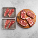 Raw steaks on metal trays and a wooden board with a gray background