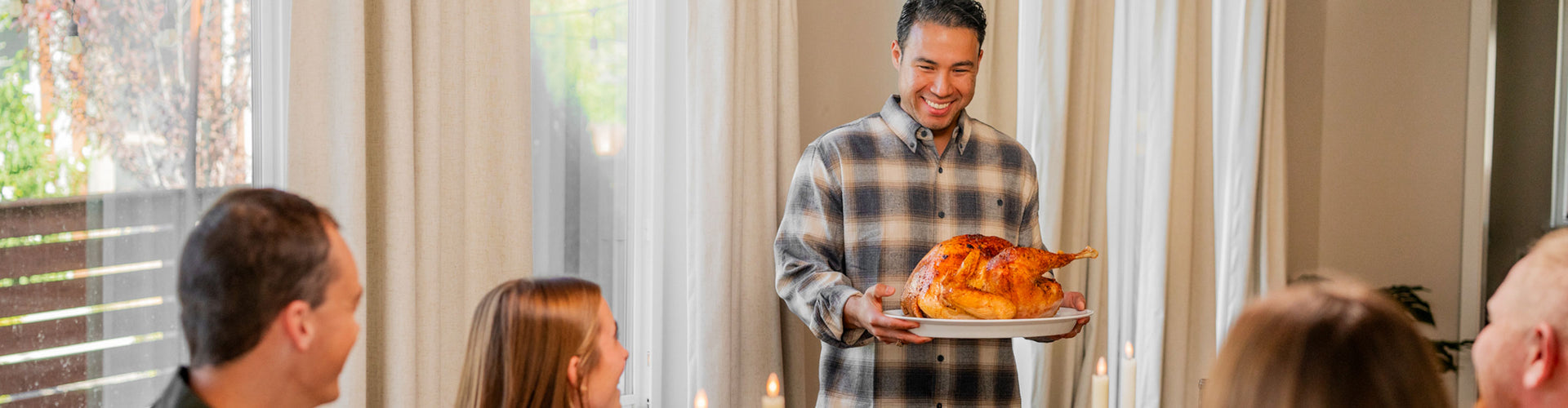Man holding a turkey with food, smiling at people inside a home.