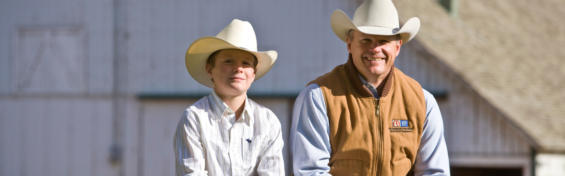 Two people wearing cowboy hats standing in front of a barn.