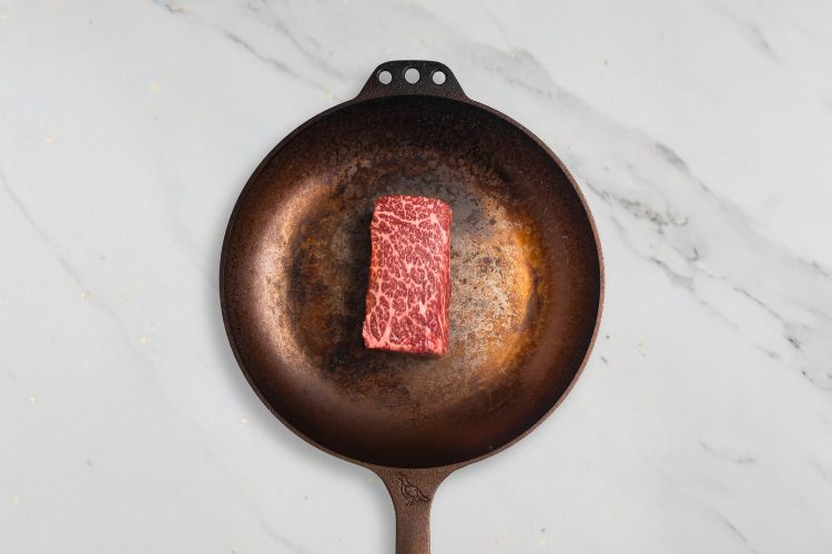 Raw steak on a hot cast iron skillet on a marble surface