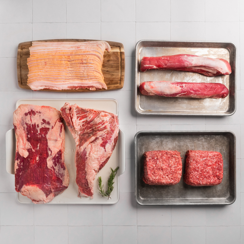 Assorted raw meats including bacon, steaks, and ground beef on a tiled surface.
