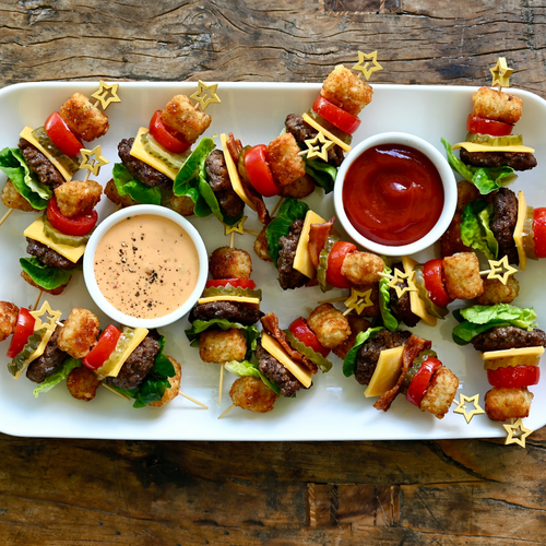 Platter of skewered mini burgers with two dips on a wooden surface