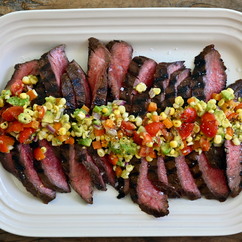 Sliced steak with a colorful corn salsa on a white platter