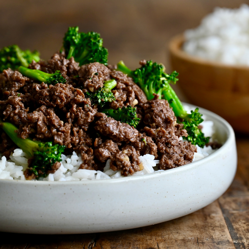 Stir-fried beef with broccoli on a bed of rice in a white bowl.