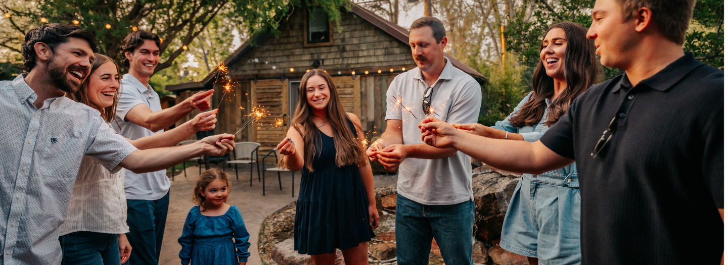 Group of people gathered outdoors near a wooden cabin, holding hands in a circle.