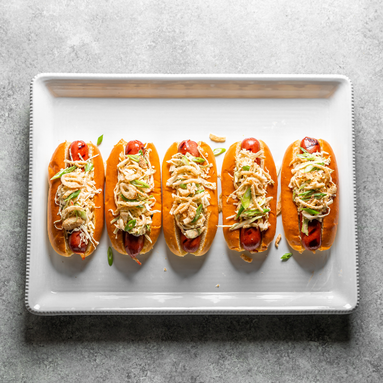 Five hot dogs with toppings on a white tray on a gray surface