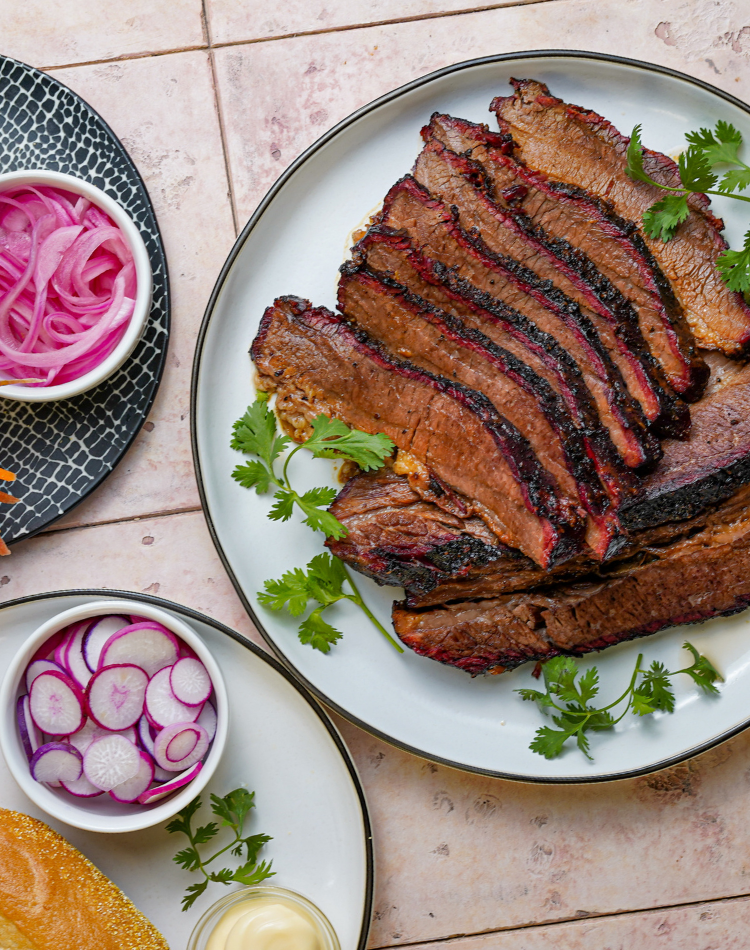 Sliced brisket on a plate with pickled vegetables and a side of bread.