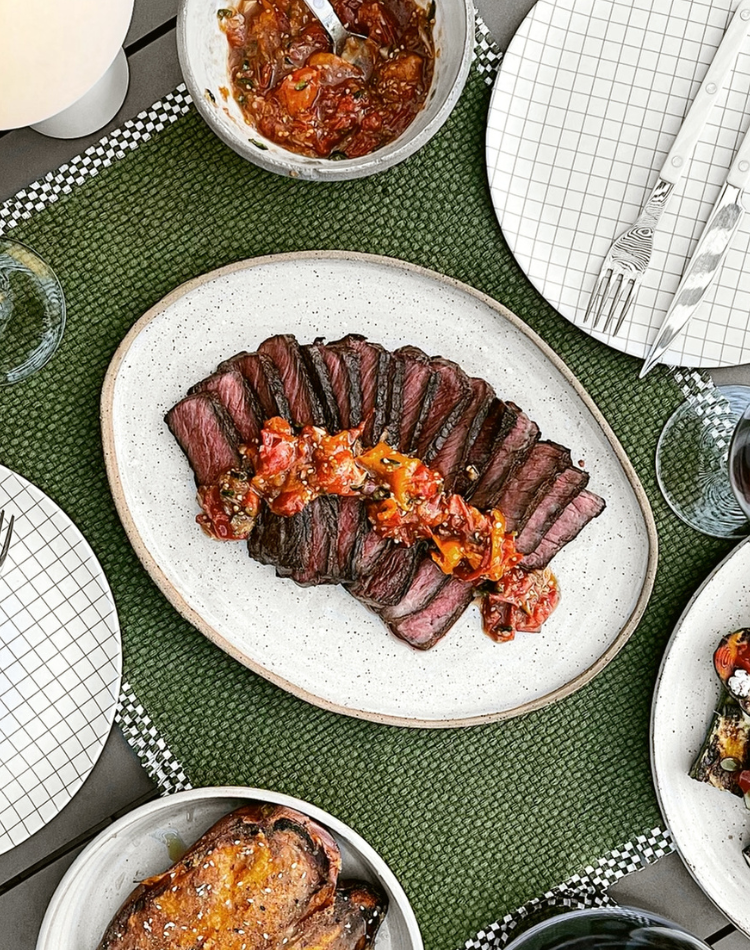 Sliced steak with tomato salsa on a white plate on a green tablecloth.