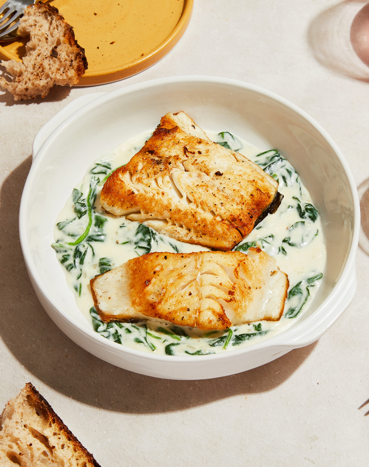 Two pieces of grilled salmon over a bed of creamy spinach in a white bowl on a light surface.