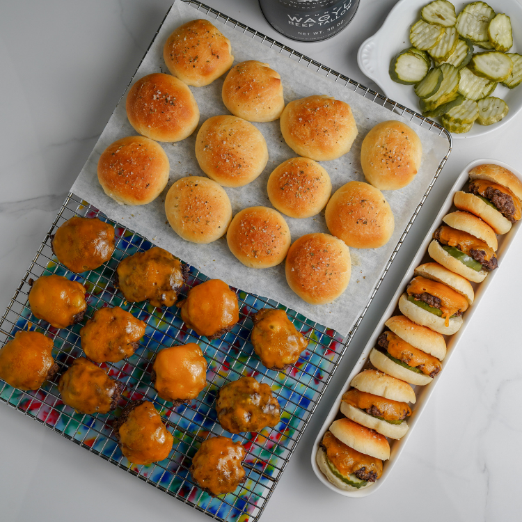 Assorted mini burgers and buns on a cooling rack with pickles on the side.