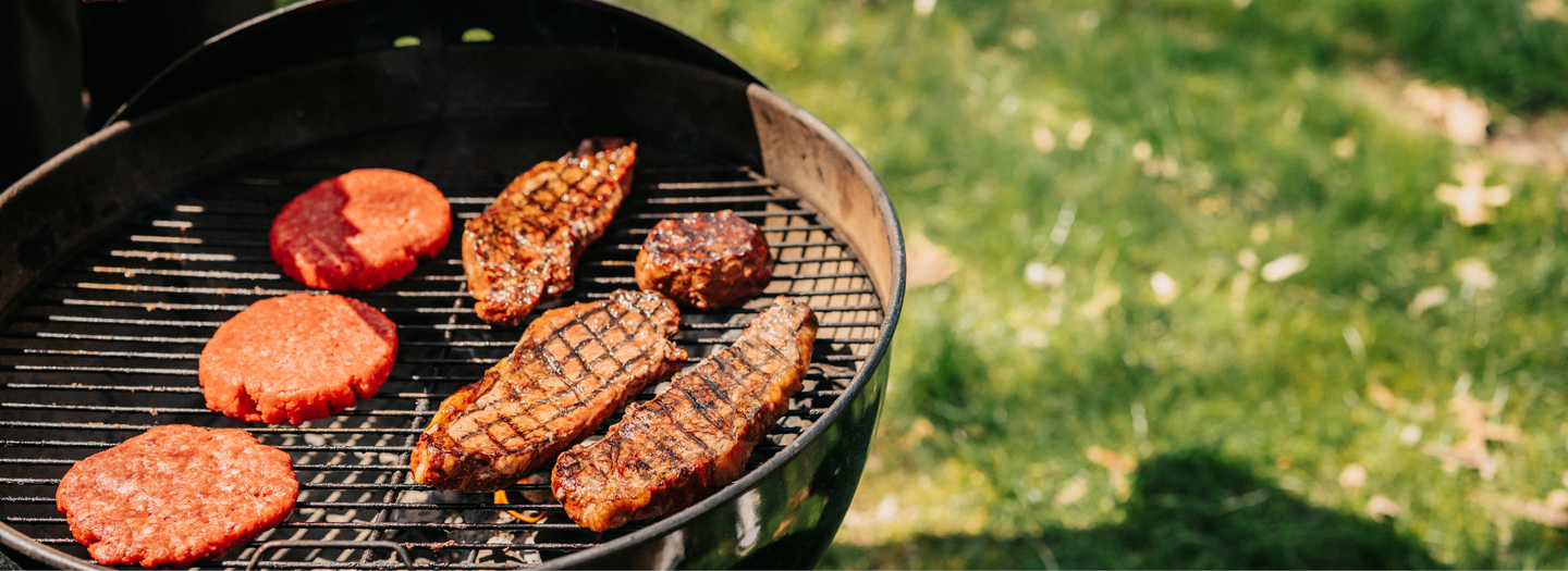 Grill with burgers and steaks cooking on a grassy outdoor background