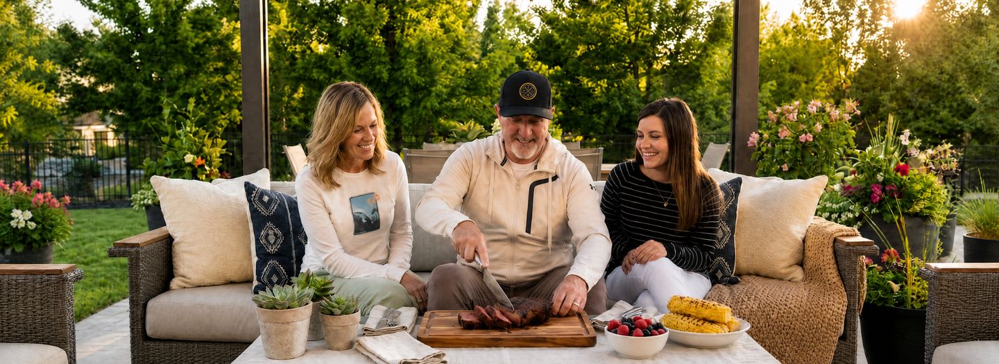 Family of three enjoying a meal outdoors on a patio with greenery and plants around.