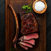 Cooked and sliced dry-aged tomahawk steak on cutting board 