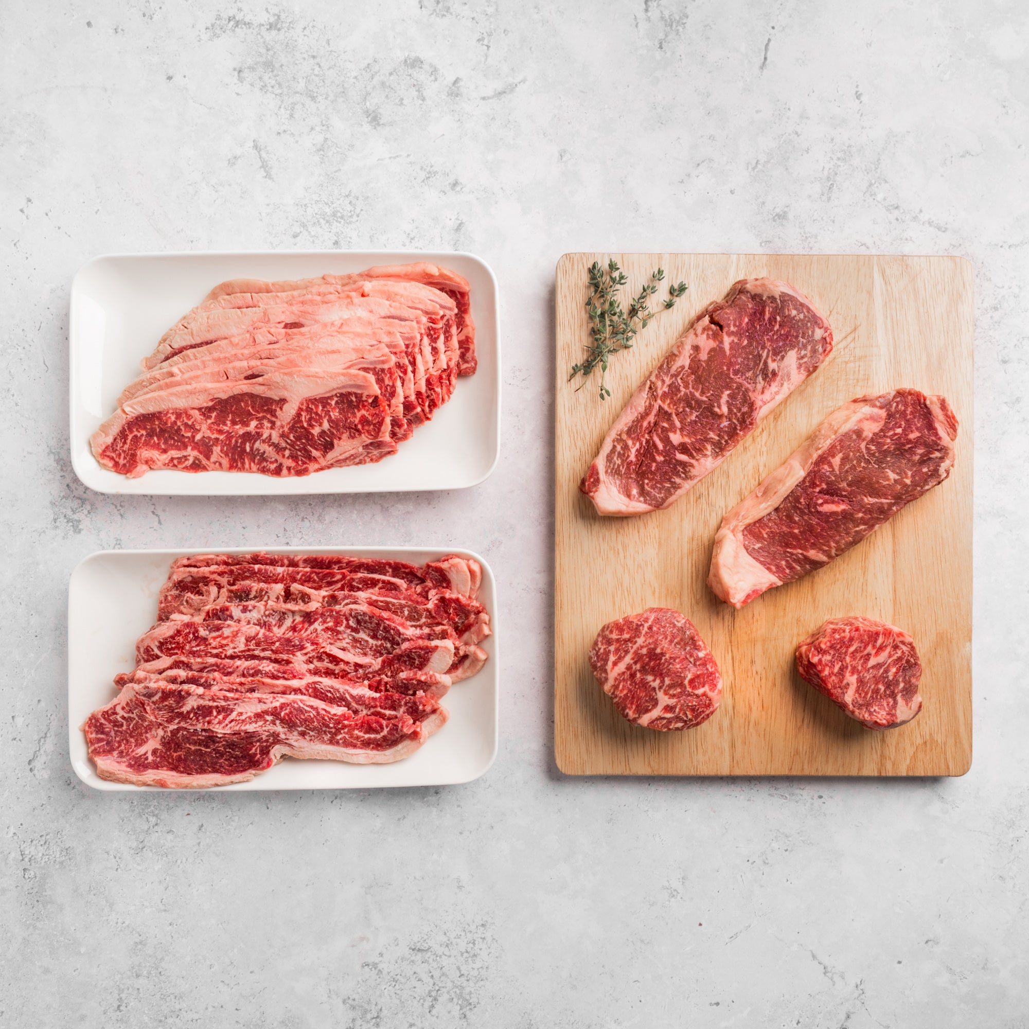 Raw steaks on a wooden cutting board and white plates with a light gray background