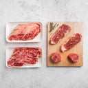 Raw steaks on a wooden cutting board and white plates with a light gray background