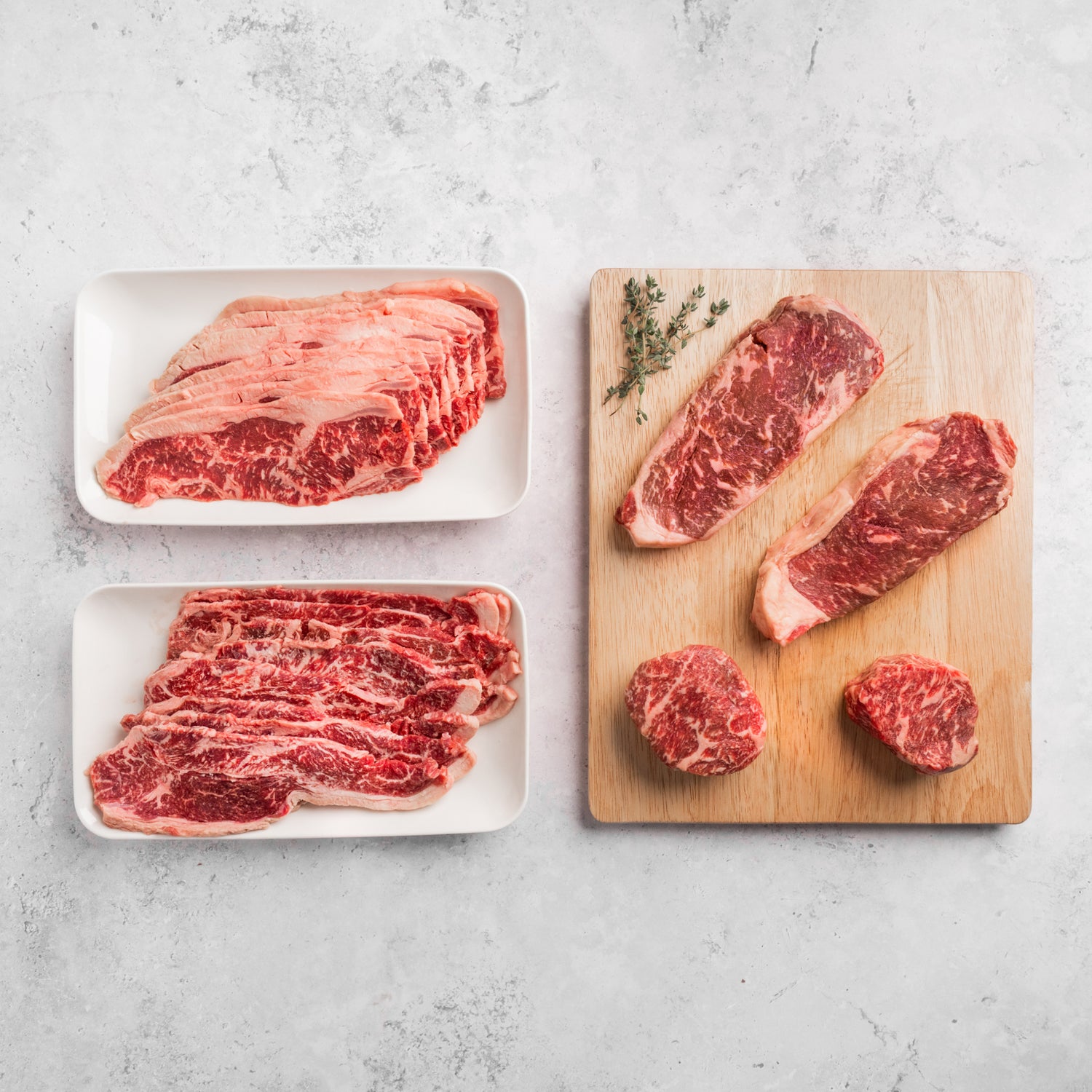Raw steaks on a wooden cutting board and white plates with a light gray background