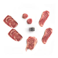 Raw steaks and meat chunks on a white background with a container of seasoning.