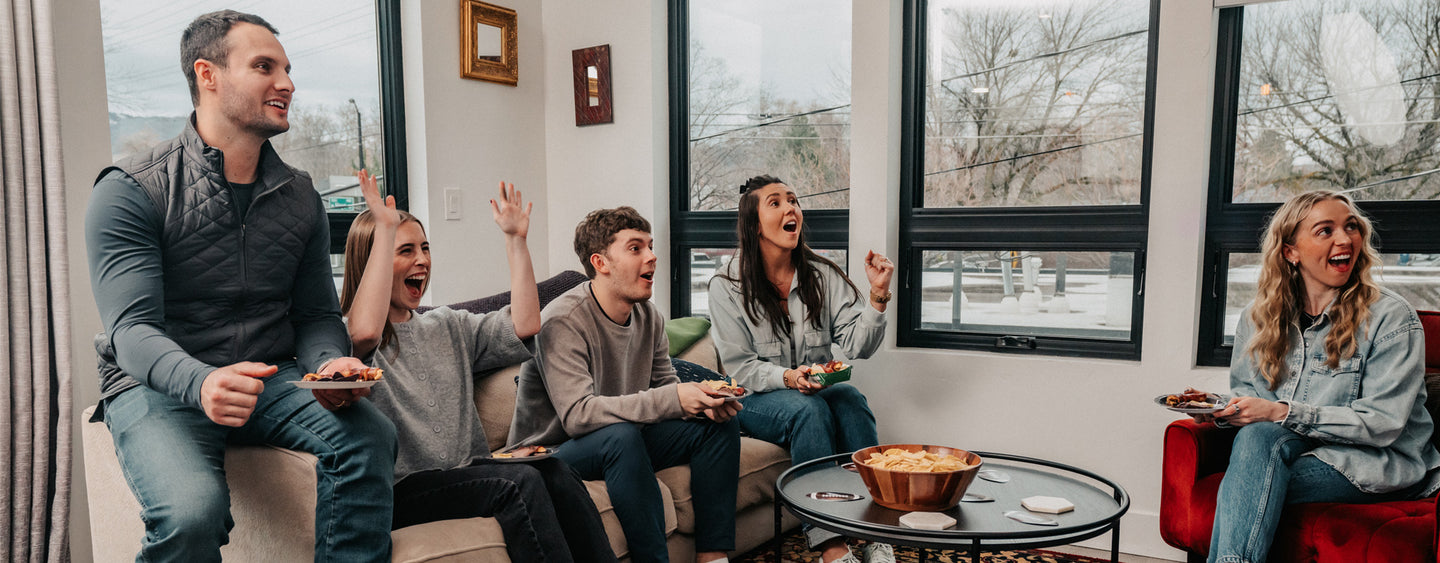 Group of people sitting on a couch in a living room, watching the big game on tv