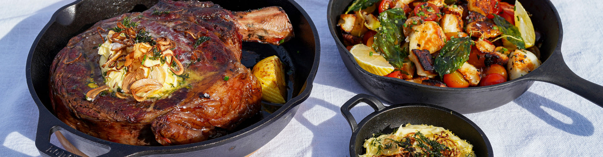Two black cast iron skillets with roasted meats and vegetables on a white surface.