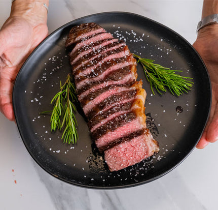 Sliced steak on a black plate with rosemary, held by two hands.