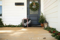 Front porch with a Christmas wreath, gift box, and small tree on a wooden deck.