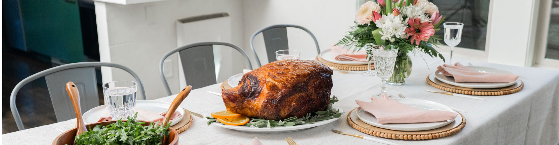 Roasted ham on a dining table with floral centerpiece and cutlery