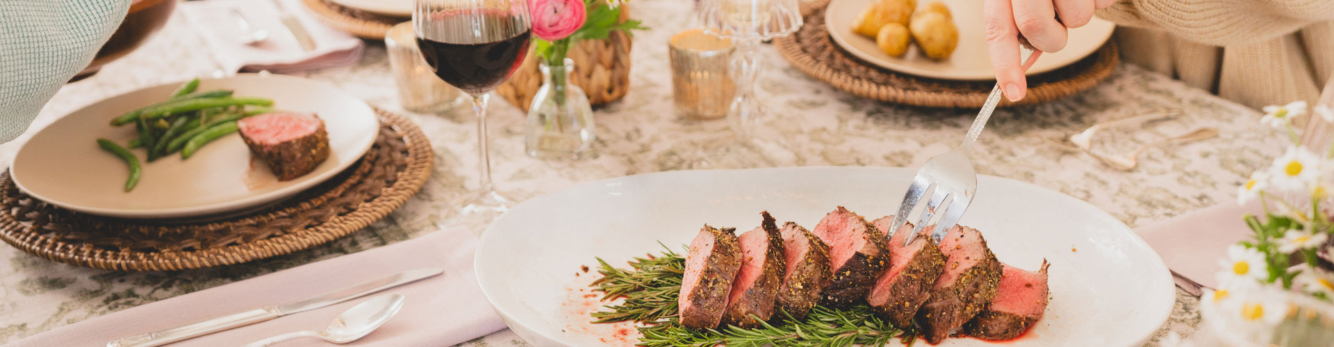 Dinner table with a plate of sliced tenderloin roast, wine glass, and cutlery.