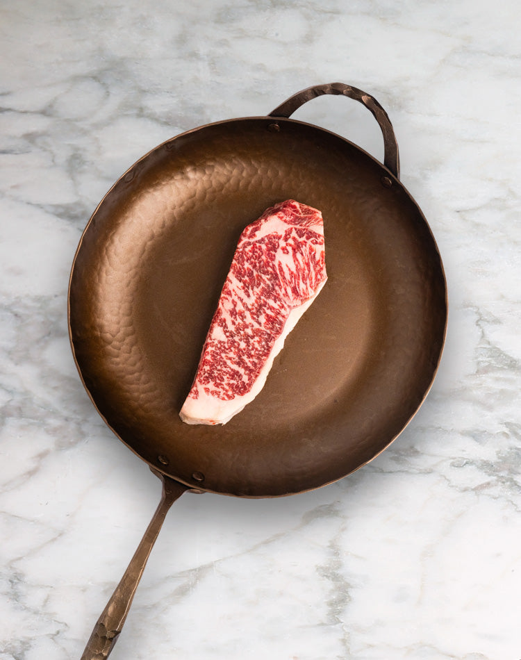 Raw steak on a brown frying pan on a marble surface