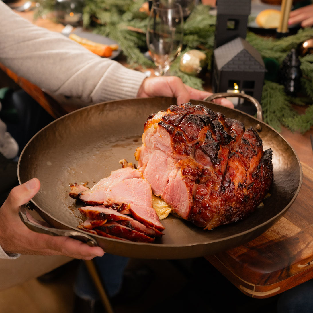 Roasted ham on a plate being held by a person in a festive setting.