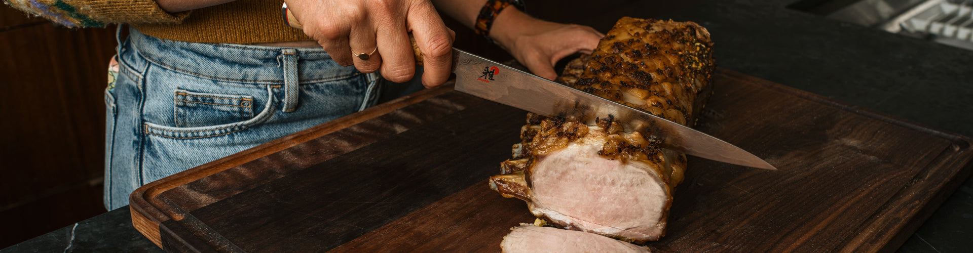 Person cutting a roasted pork loin on a wooden cutting board with a knife.