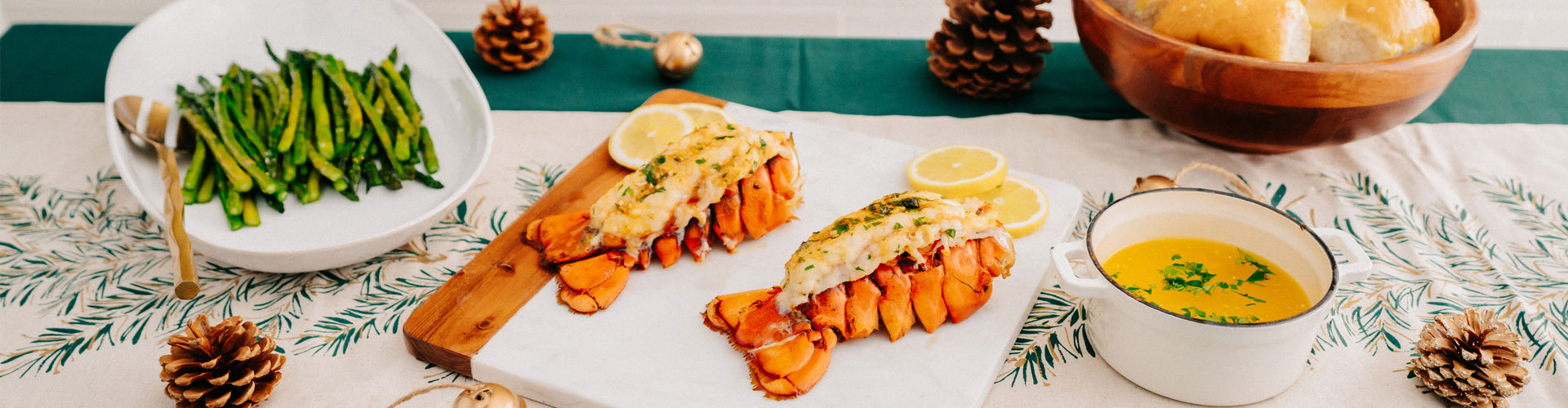 Dinner table with lobster tails, asparagus, and a bowl of sauce on a decorative tablecloth.