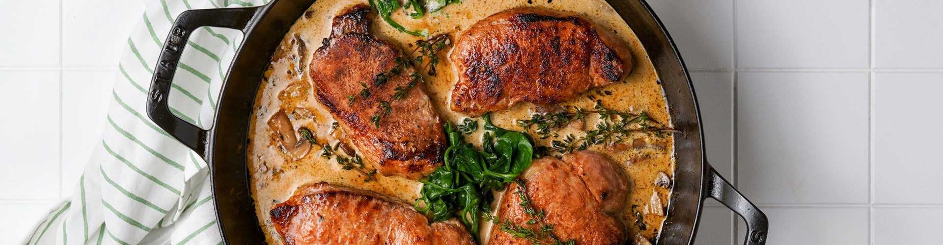 Baked pork chops with herbs in a skillet on a tiled surface
