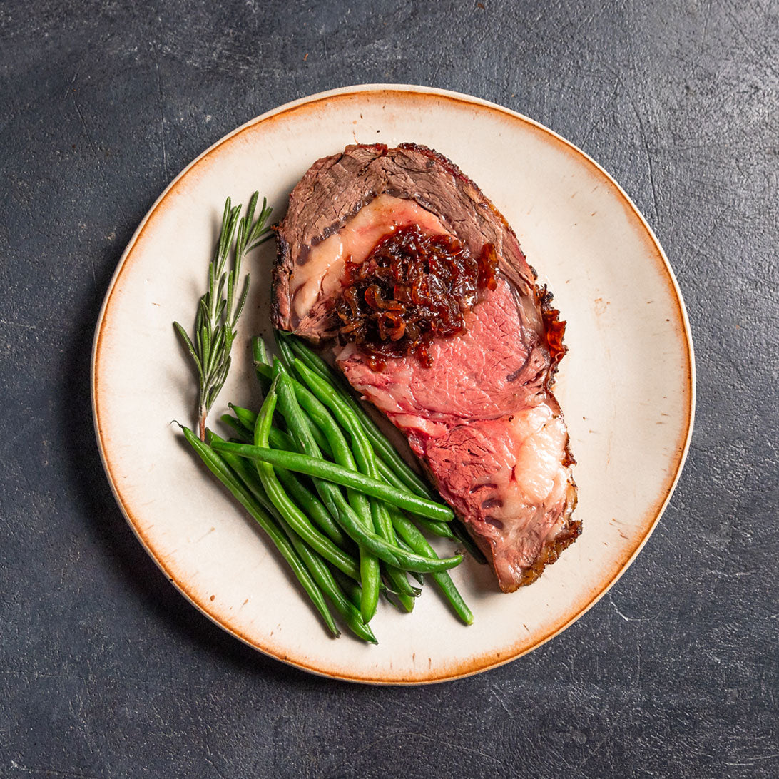 Roast prime rib beef with green beans on a white plate with a dark background