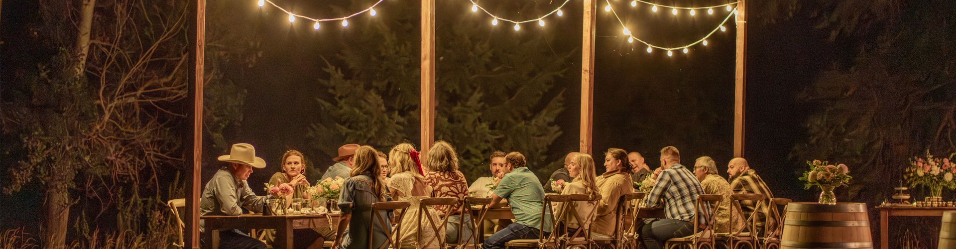Group of people sitting around a table under string lights at night.