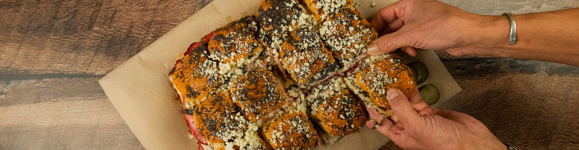 Person pulling apart Kurobuta ham Hawaiian roll sandwiches