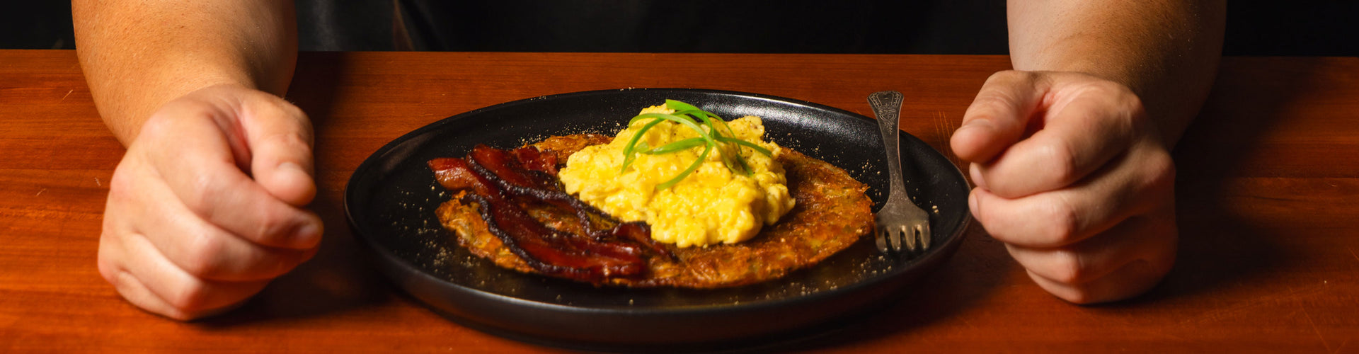 Plate of food with scrambled eggs, bacon, and toast on a wooden table.