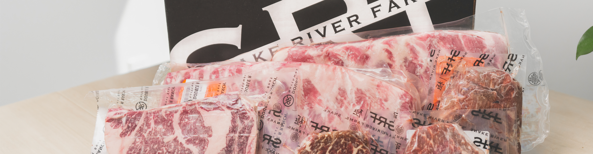 Packaged meat products on a table with a 'Snake River Farm' box in the background.