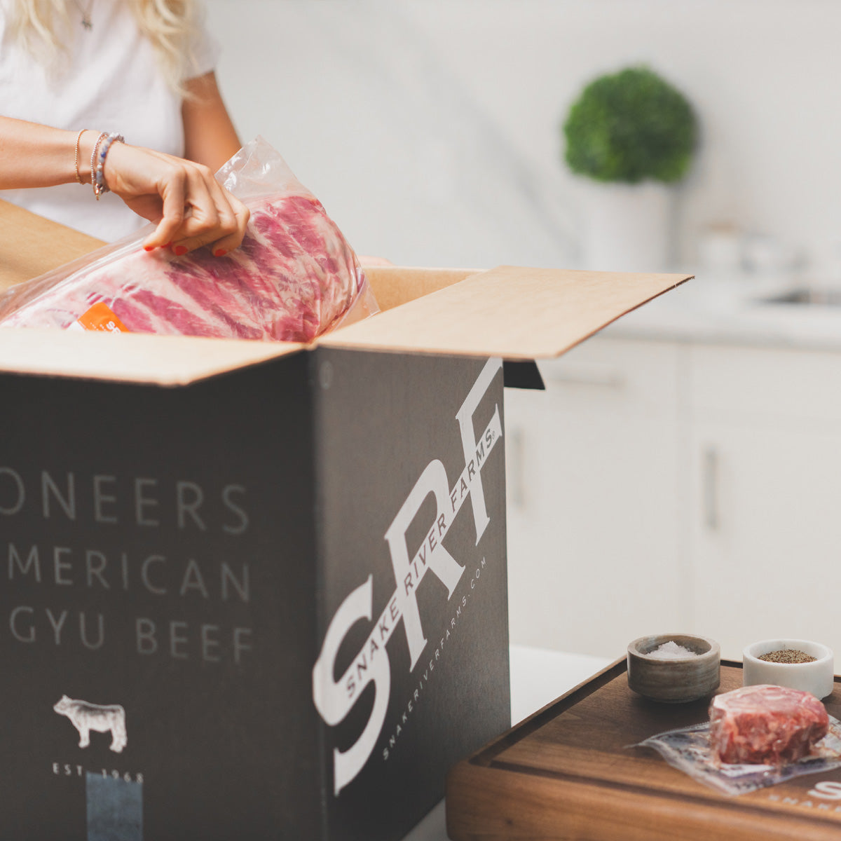 Person opening a box of SRF American Wagyu Beef in a kitchen setting.
