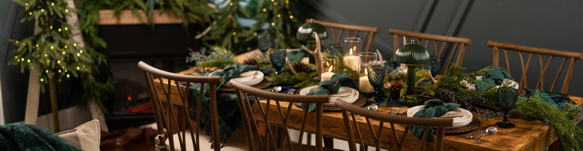 Dining table set for a meal with greenery and candles in a cozy indoor setting.