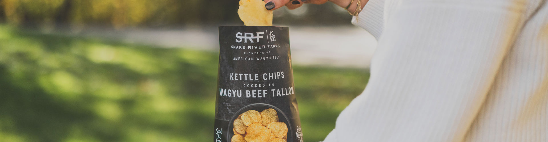 Person holding a can of SRF kettle chips with a blurred outdoor background