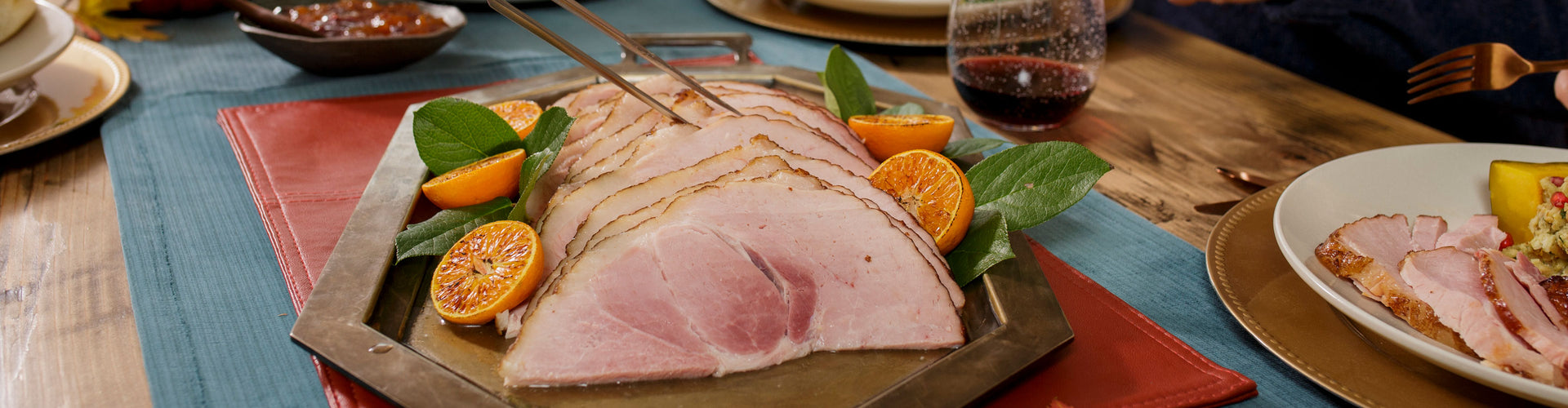 Sliced ham on a platter with garnishes on a table setting.