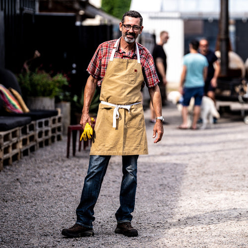 Man wearing a brown apron standing outdoors with blurred background